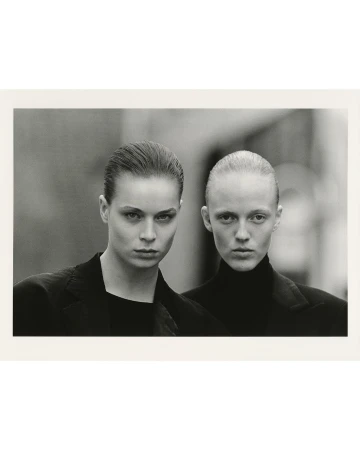 Monochrome portrait of two women in black jackets, close-up shot with blurred background, serious expressions, and slicked-back hairstyles.