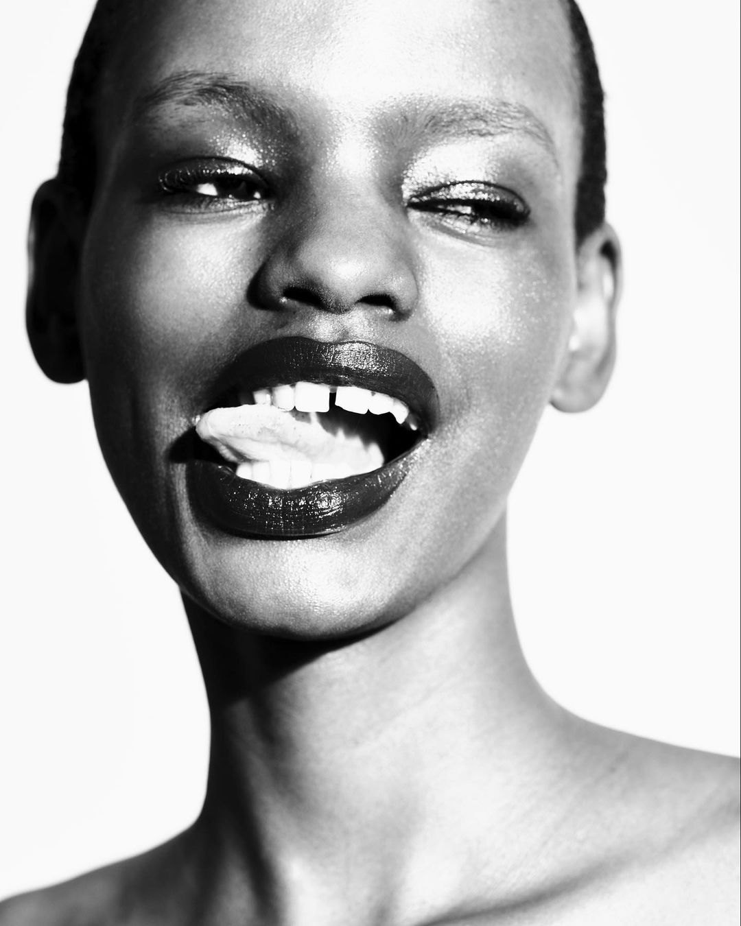 Close-up black and white portrait of a happy African woman with her tongue sticking out and a slight smile on her face.
