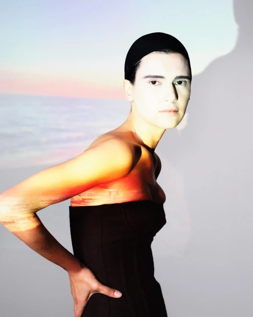 Studio shot of a woman in a black dress against a gradient sunset background, showcasing fashion and artistic photography.
