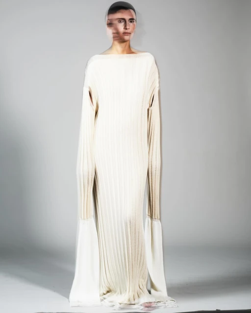 Woman poses in a full-length, ribbed, light beige dress with sleeves that extend into long, flowing, off-white fabric extensions.