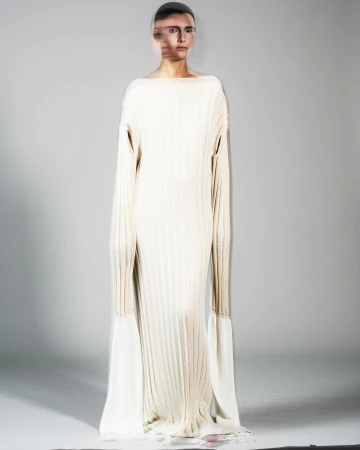 Woman poses in a full-length, ribbed, light beige dress with sleeves that extend into long, flowing, off-white fabric extensions.
