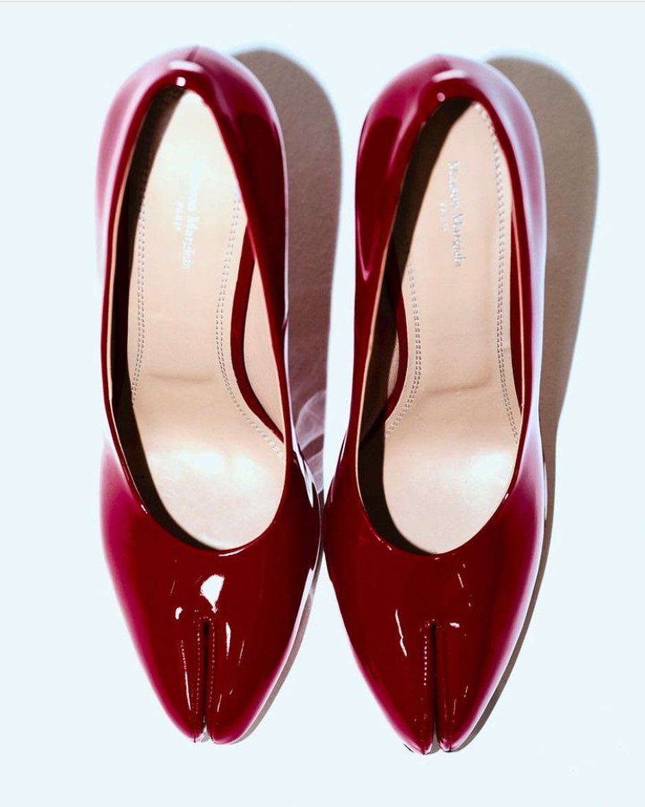 Pair of glossy, dark red high-heel shoes on a white background, featuring a distinctive split-toe design; studio shot with soft shadows.