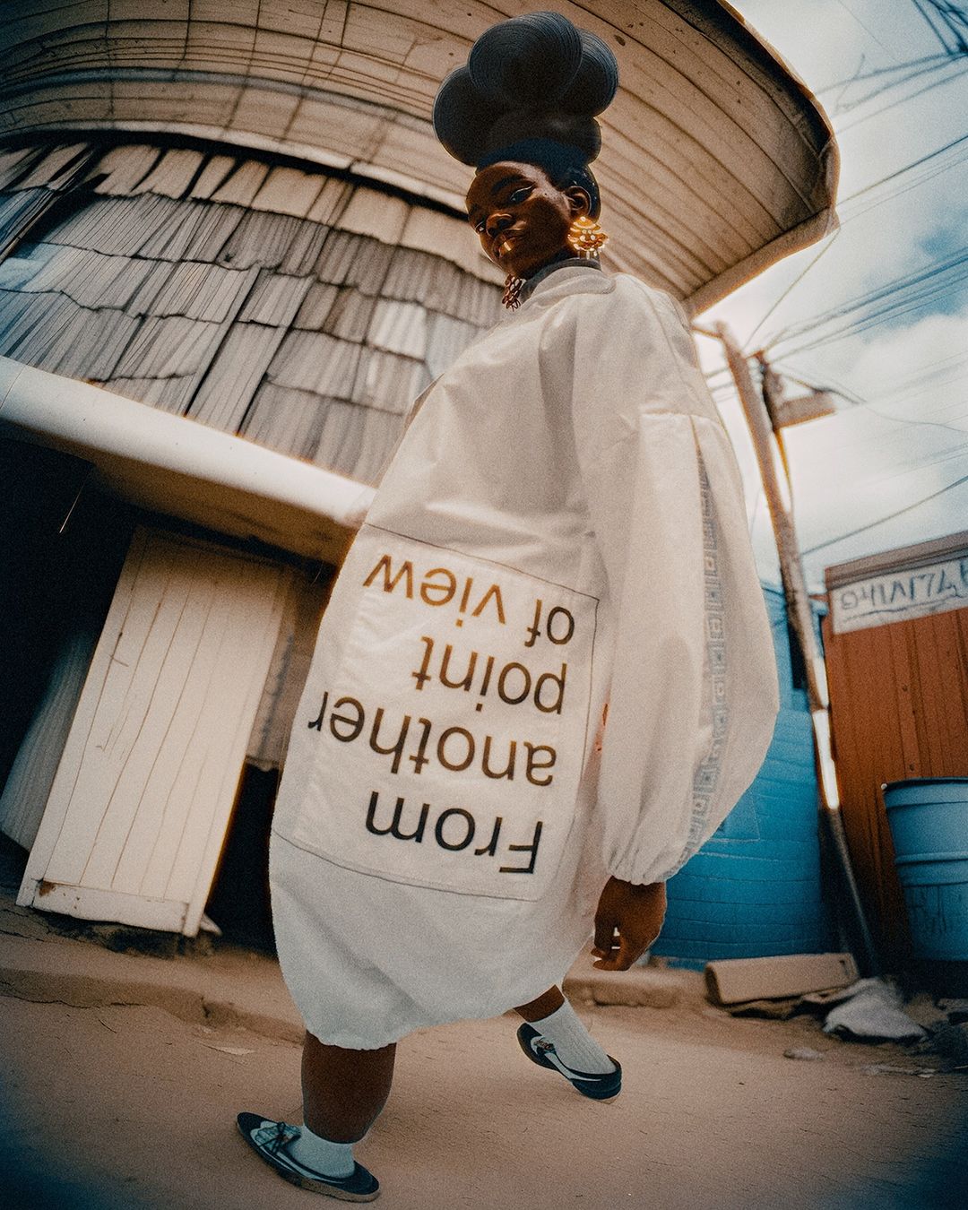 A stylish Black woman with a unique hairstyle, wearing an oversized white coat, gold earrings, and distinctive shoes, poses in an urban setting.