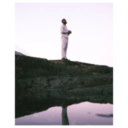 A man standing on a rocky outcrop near water by photographer Dune Tilley in Cape Town