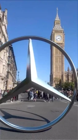 Mercedes-Benz logo sculpture in front of Elizabeth Tower (Big Ben) at the Palace of Westminster in London on a sunny day.