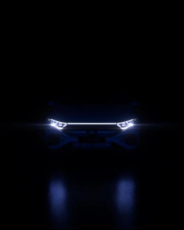 Front view of a car with illuminated headlights and grill in a dark setting, creating a sense of mystery and highlighting the vehicle's design.