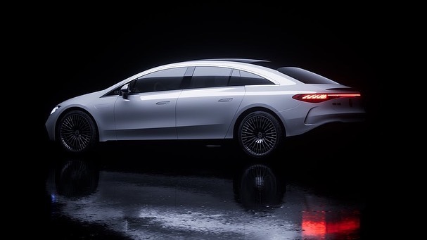 Sleek silver Mercedes-Benz EQS sedan in a studio environment with a dark backdrop and reflective floor, showcasing automotive design.
