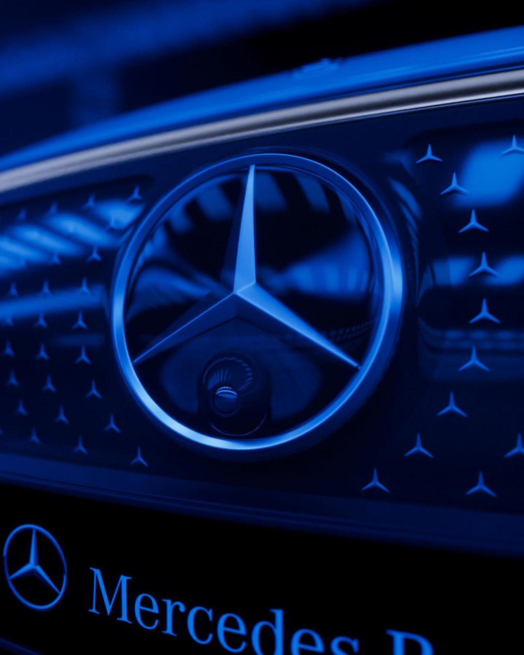 Close-up of a blue Mercedes-Benz emblem on a car grille with a repeating star pattern. Automobile branding with a luxury aesthetic.