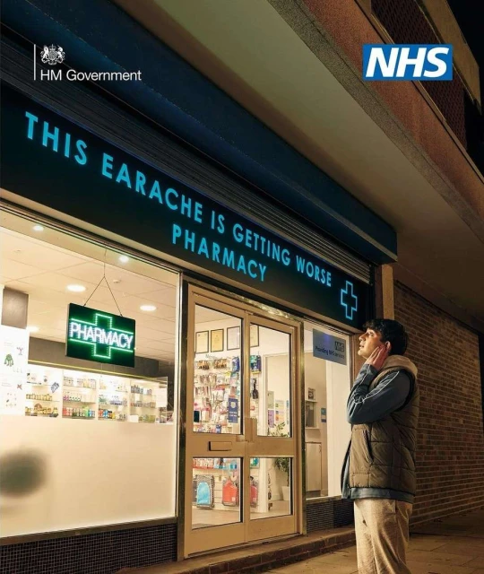 Man in vest outside a pharmacy at night under a sign with text: 'This earache is getting worse'. The pharmacy is lit up at night.