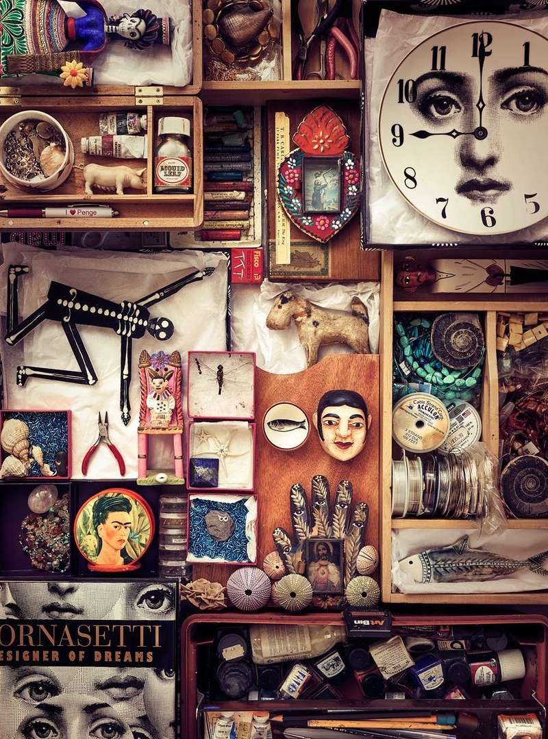 Collection of vintage art and design objects arranged in wooden boxes. Includes a clock with a face, dolls, figurines, and art prints.