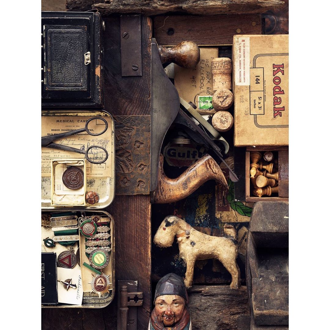 An overhead studio shot shows a variety of vintage objects including an antique camera, a wood plane, and an old Kodak box. Chess pieces are also visible.