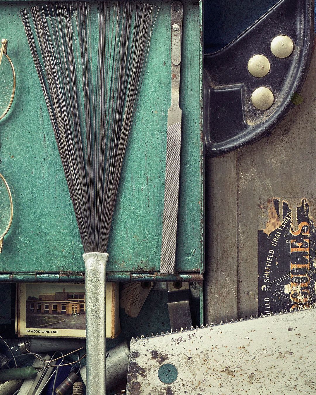 Close-up still life showcasing a collection of vintage tools and hardware with glasses, a file, a broom, and a rusty metal box.