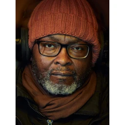 Portrait of a Black man with glasses and a red beanie wearing headphones by Dylan Collard