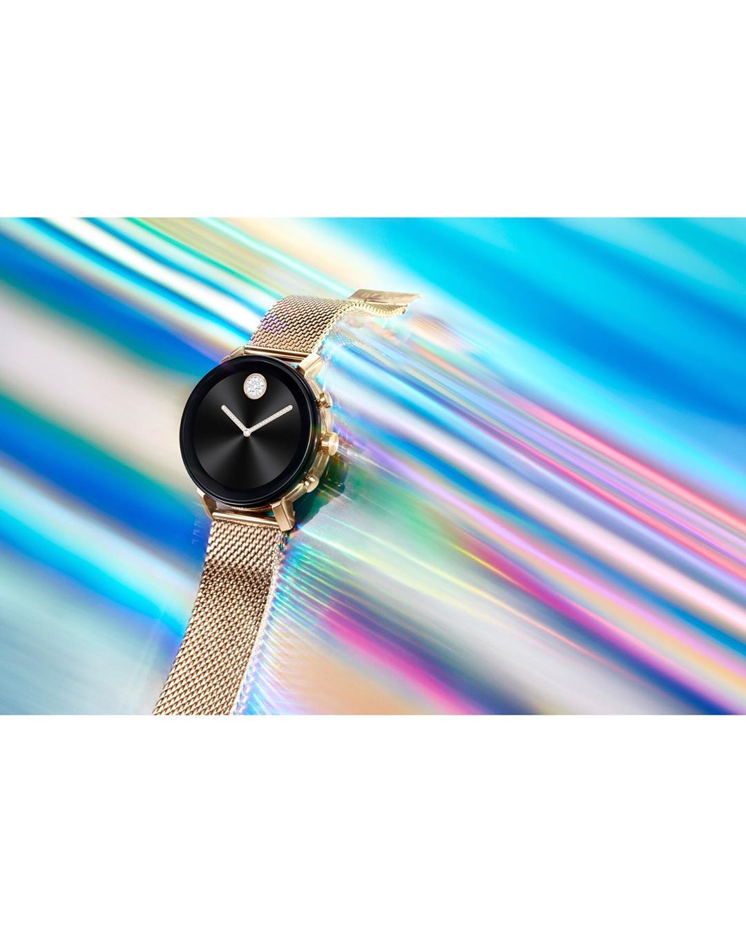 Close-up studio shot of a gold wristwatch with a black face set against a colorful, blurred light streak background.