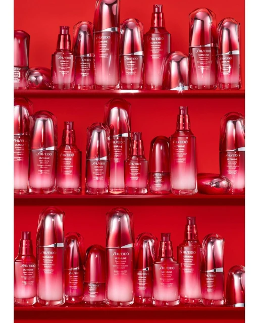 An array of red and white SHISEIDO ULTIMUNE skincare product bottles displayed on three shelves in a brightly lit studio environment.