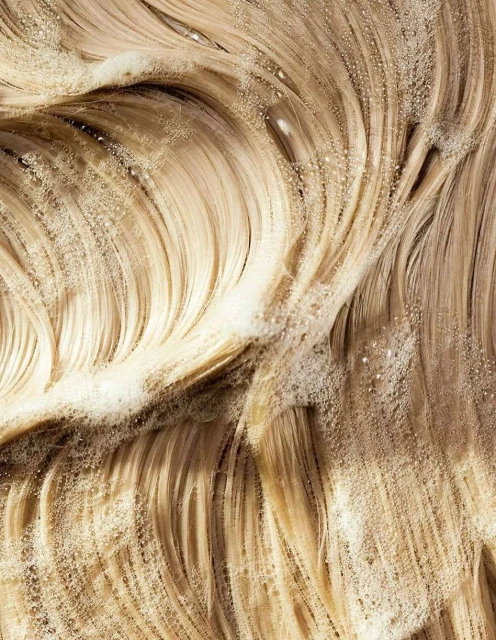 Close-up of wavy blonde hair with white shampoo lather, highlighting texture and color, ideal for beauty and haircare searches.