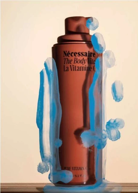 Necessaire brand body vitamin C bottle in studio setting, surrounded by blue paint, against a beige backdrop, beauty and skincare concept.