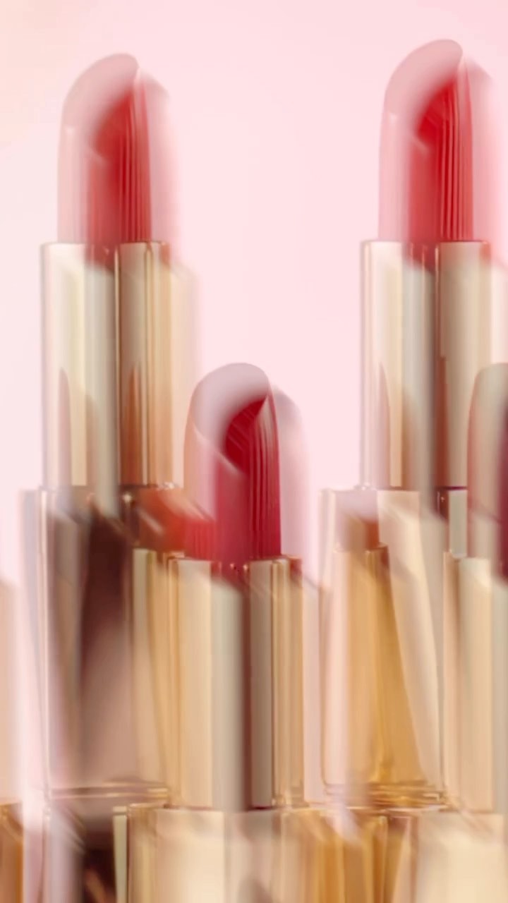 Close-up of multiple lipsticks against a pale pink background with soft motion blur effects