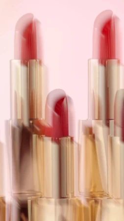 Close-up of multiple lipsticks against a pale pink background with soft motion blur effects