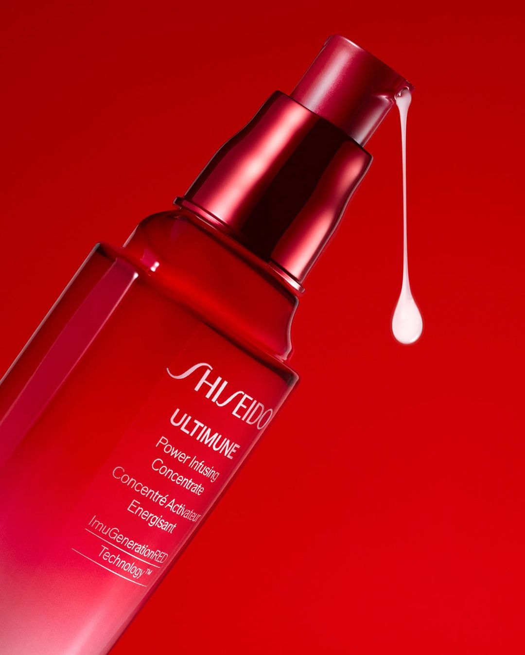 Red Shiseido Ultimune power infusing concentrate bottle with a drop of liquid serum on a vivid red background in a close-up product shot.