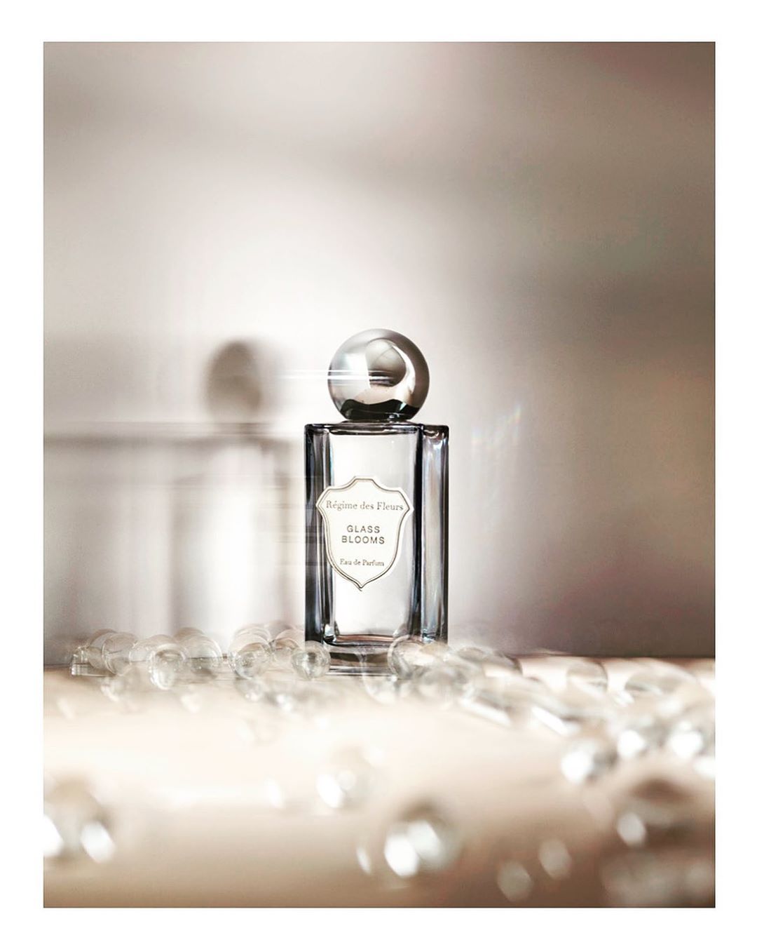 Elegant still life shot of a glass perfume bottle with a round cap, with decorative glass beads on a soft surface in a warm-toned setting.