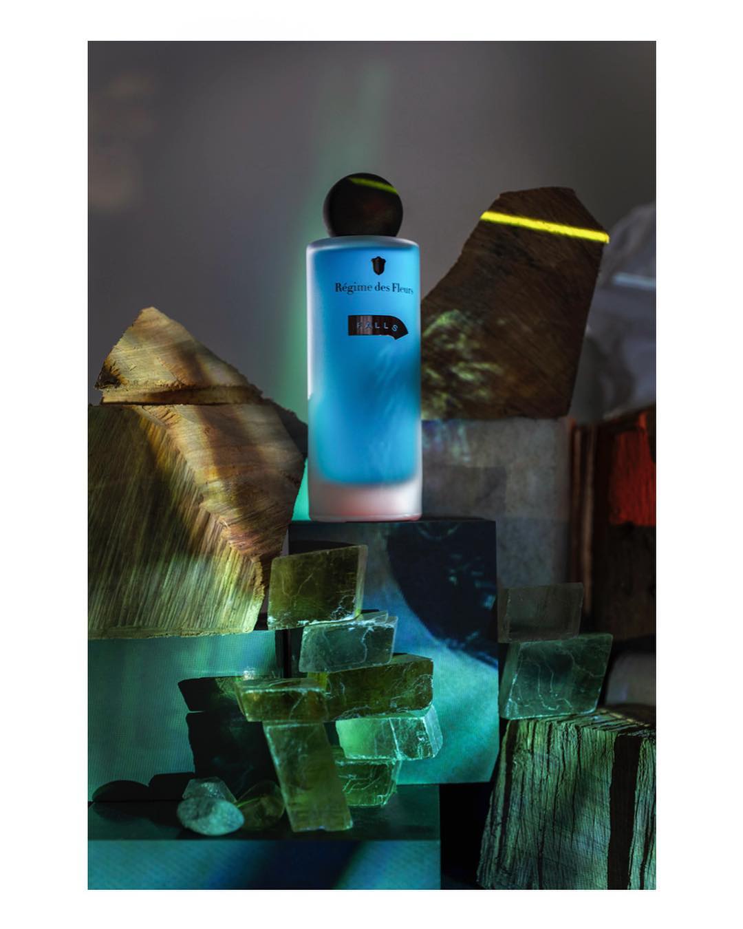 Artistic studio shot of a blue perfume bottle among wood and stone blocks, showcasing textures and geometric shapes with moody lighting.