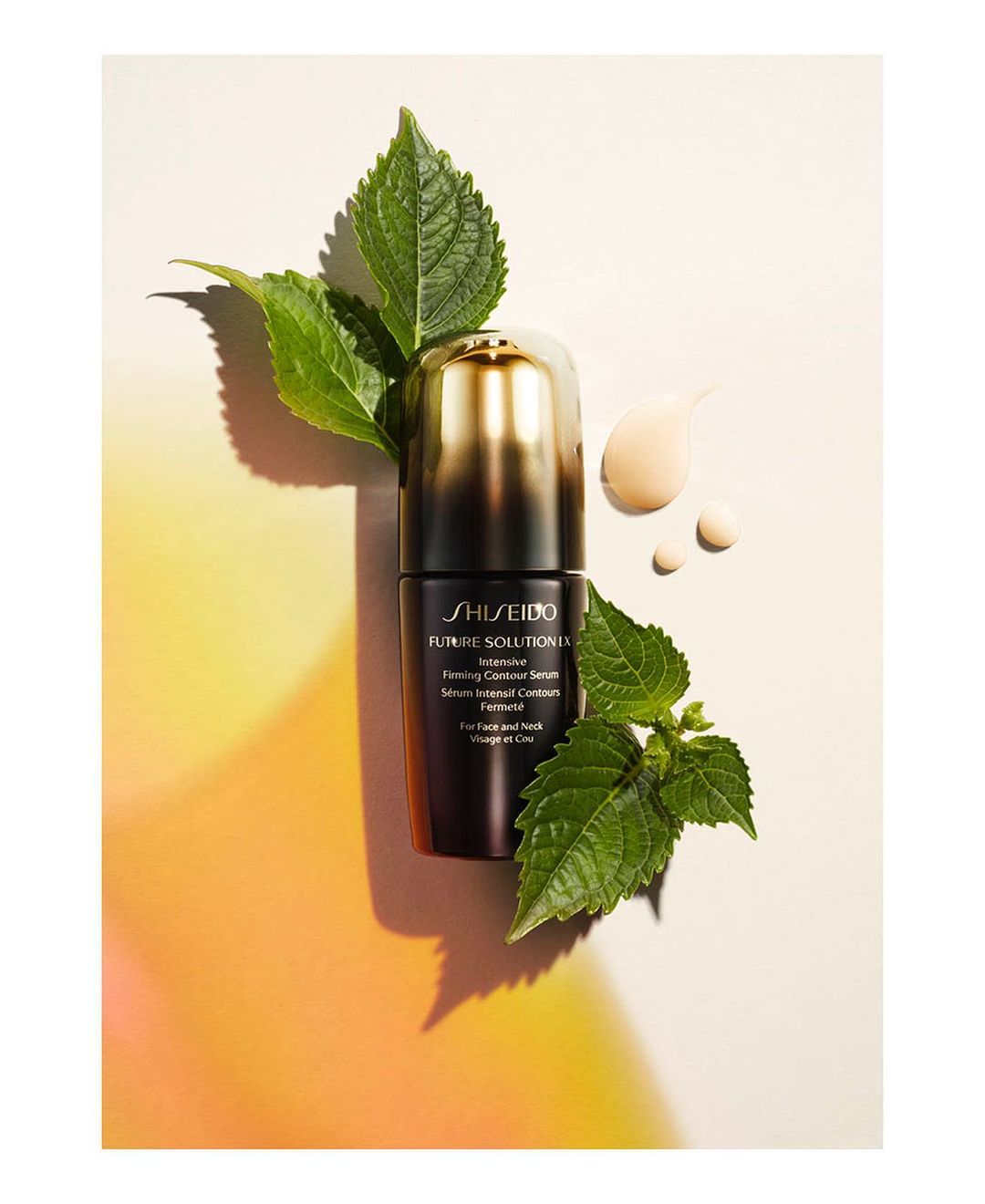 Product shot of Shiseido Future Solution LX Intensive Firming Contour Serum with green leaves and cream colored serum drops in studio.