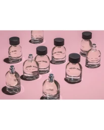 Multiple clear glass perfume bottles with black and silver caps arranged on a solid pink backdrop