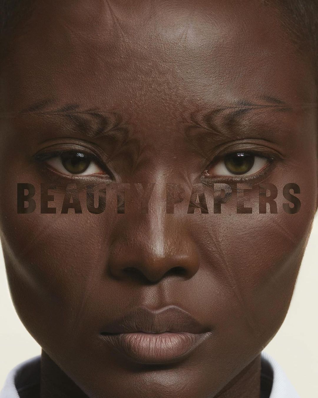 Close-up portrait of a woman of African descent with dark skin, a serious expression, and the text 'BEAUTY PAPERS' overlaid on her face.