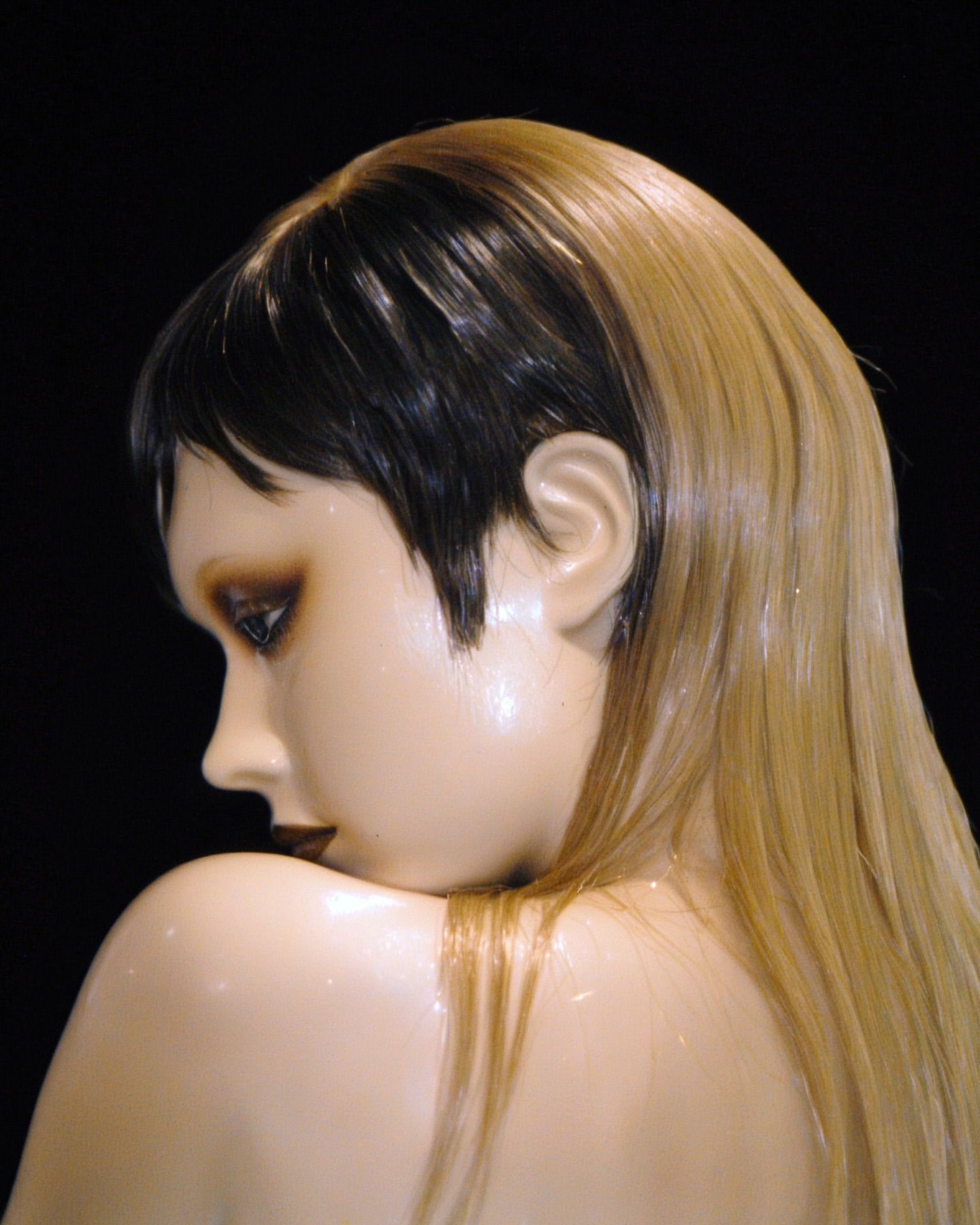Profile of a mannequin head with two-tone dark and blonde hair against a black background, showcasing hair and beauty concepts.