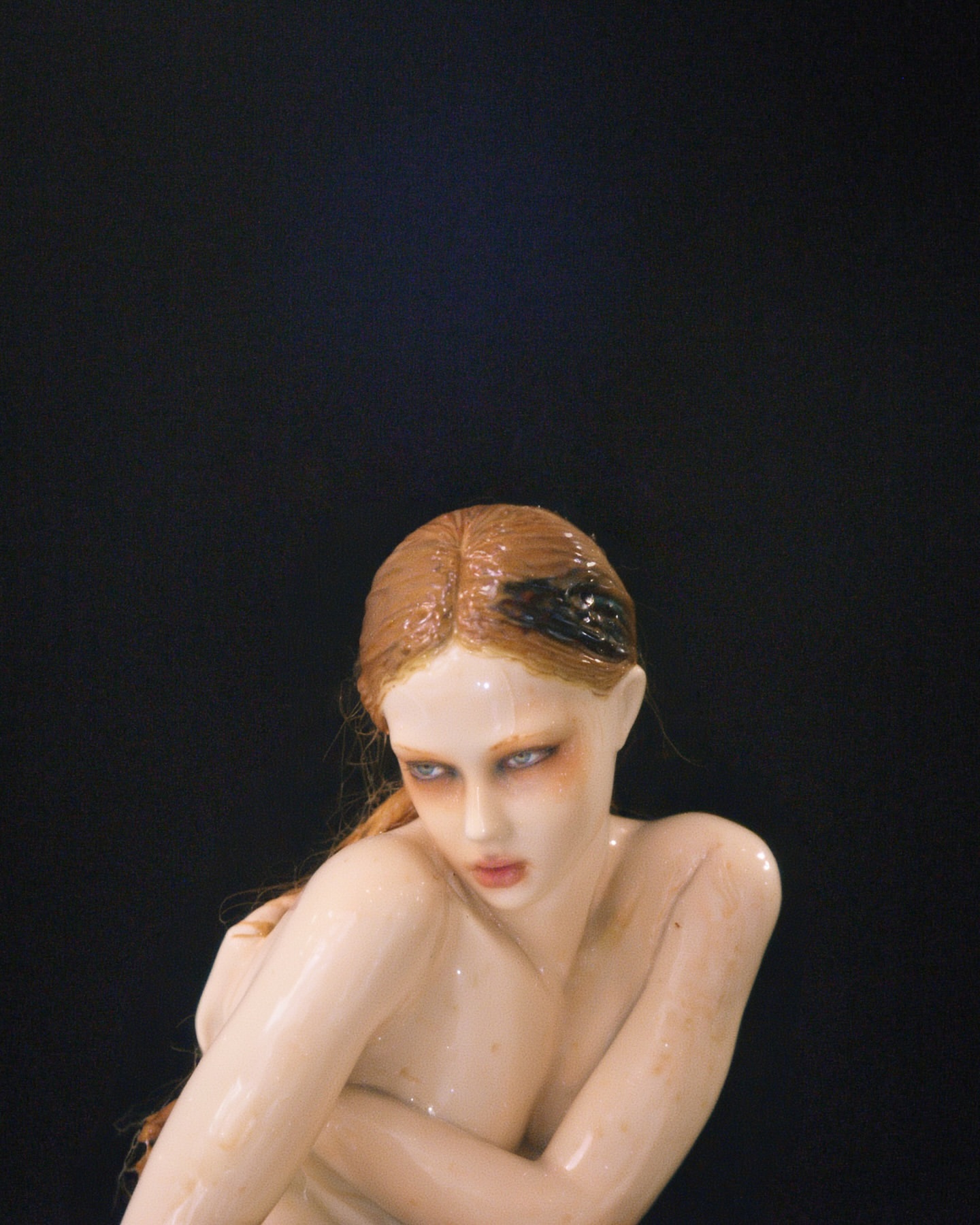 Artistic studio shot of a bare-shouldered woman with red hair and fair skin, posed against a dark backdrop, creating a dramatic and alluring effect.