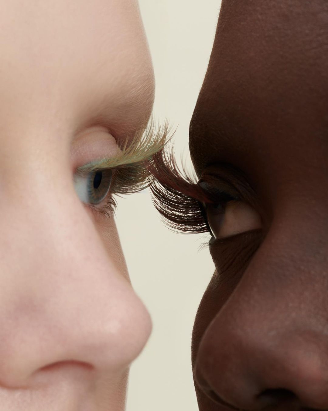 Close-up of two adults of different ethnicities with colorful false eyelashes touching in a beauty or fashion context.