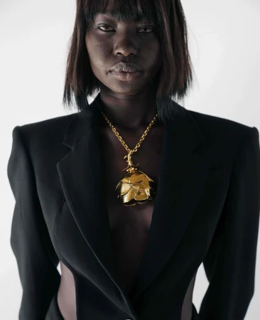 Fashion shot of a Black woman in a black blazer with a gold rose necklace in a studio, striking a pose against a white backdrop.