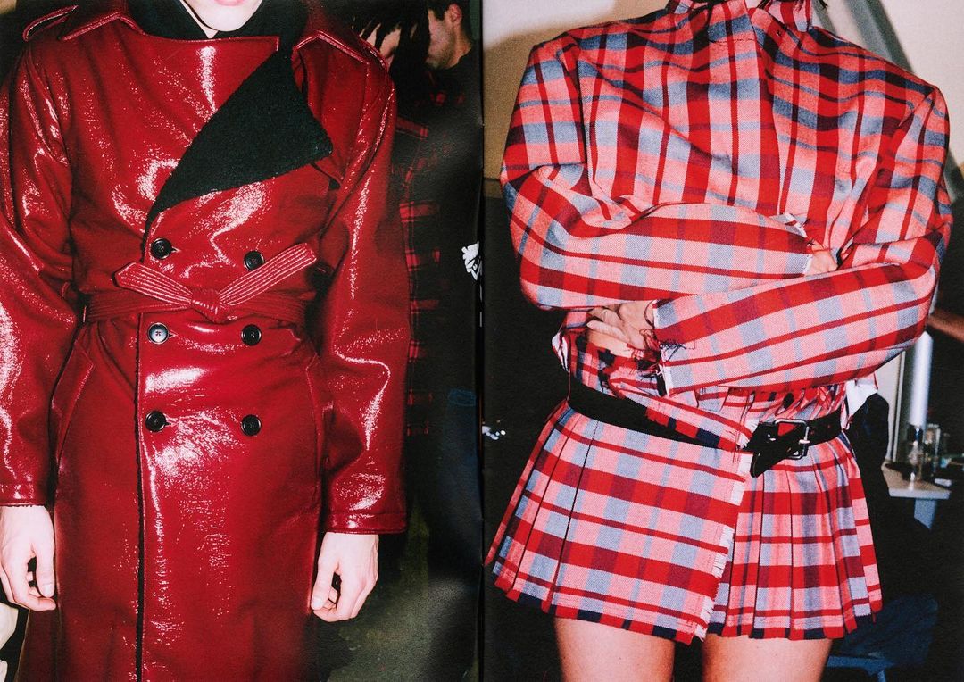 Close-up of two fashion models showcasing a shiny red belted coat and a red, grey, and white plaid kilt with matching top.