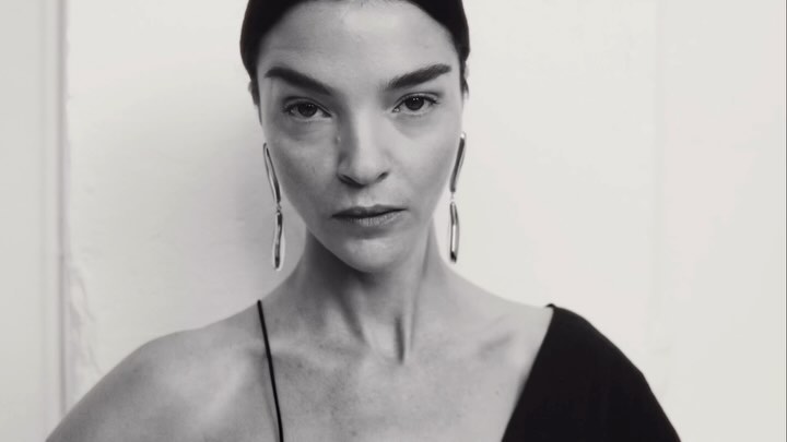 Close-up portrait of a woman wearing long silver earrings and a black top against a plain light background