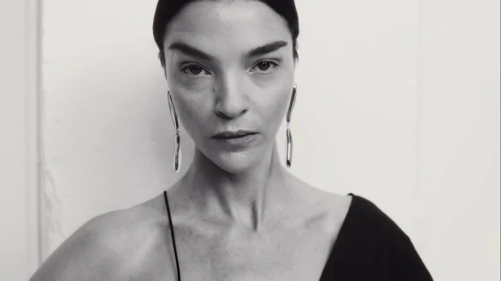 Close-up portrait of a woman wearing long silver earrings and a black top against a plain light background