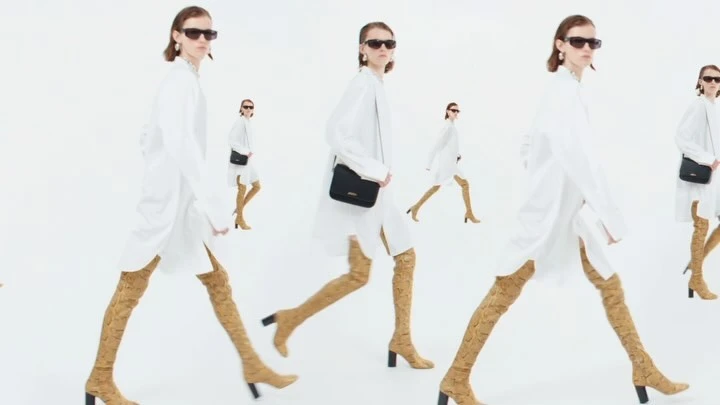 Fashion shoot featuring multiple models in white dresses, thigh-high snake print boots, and sunglasses walking against a bright white backdrop.
