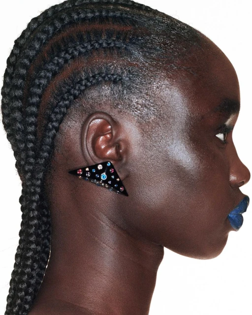Profile portrait of a black female adult wearing a triangular black statement earring with colorful gems and dark blue lipstick. 