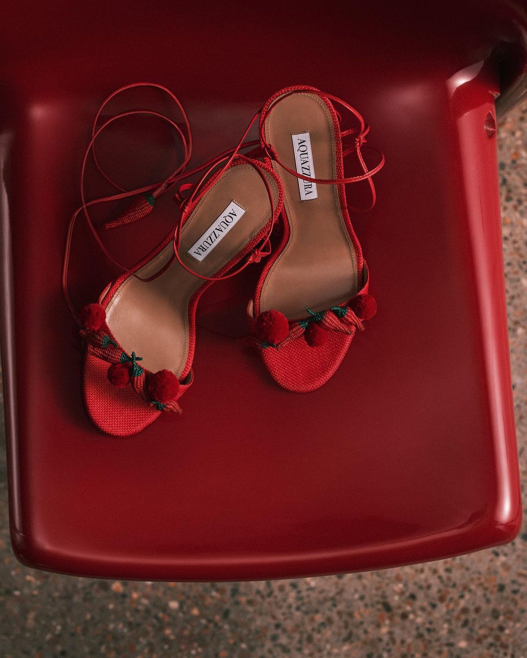 Red Aquazzura sandals with pompom details on a red seat create a bold, fashionable statement for summer footwear.