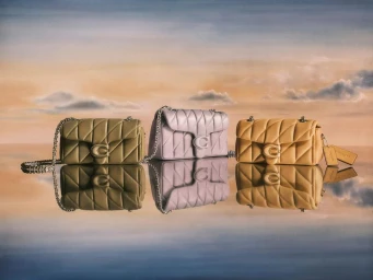 Three quilted leather handbags in olive green, lilac, and tan displayed on a reflective surface against a painted cloudy sky backdrop