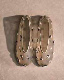 Top-down view of a pair of sheer mesh ballet flats with embroidered white and purple flowers against a textured light backdrop.