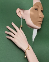 Close-up portrait of a woman wearing gold pearl jewelry framed through a torn green paper backdrop by photographer Edwin Ho.
