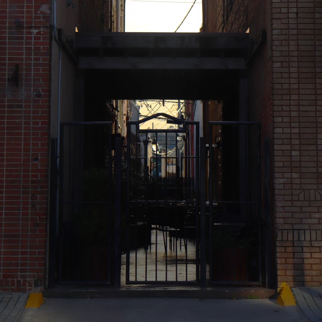 Exterior shot of a dark alleyway with a metal gate, brick walls, and limited visibility, creating a somewhat mysterious urban environment.