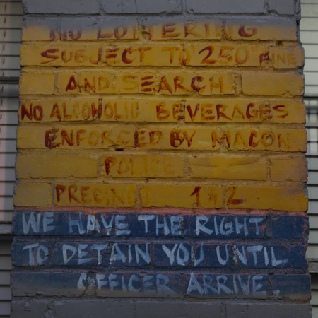 Weathered brick wall covered in painted legal warnings and notices in red, white, and blue; public space and signage.