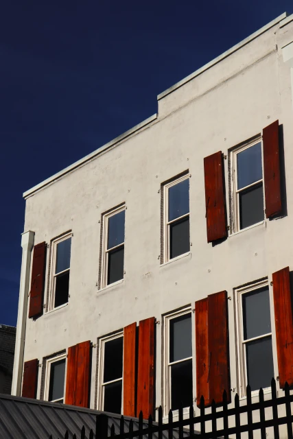 Exterior of an off-white building with multiple windows and brown shutters on a sunny day, viewed from a low angle.