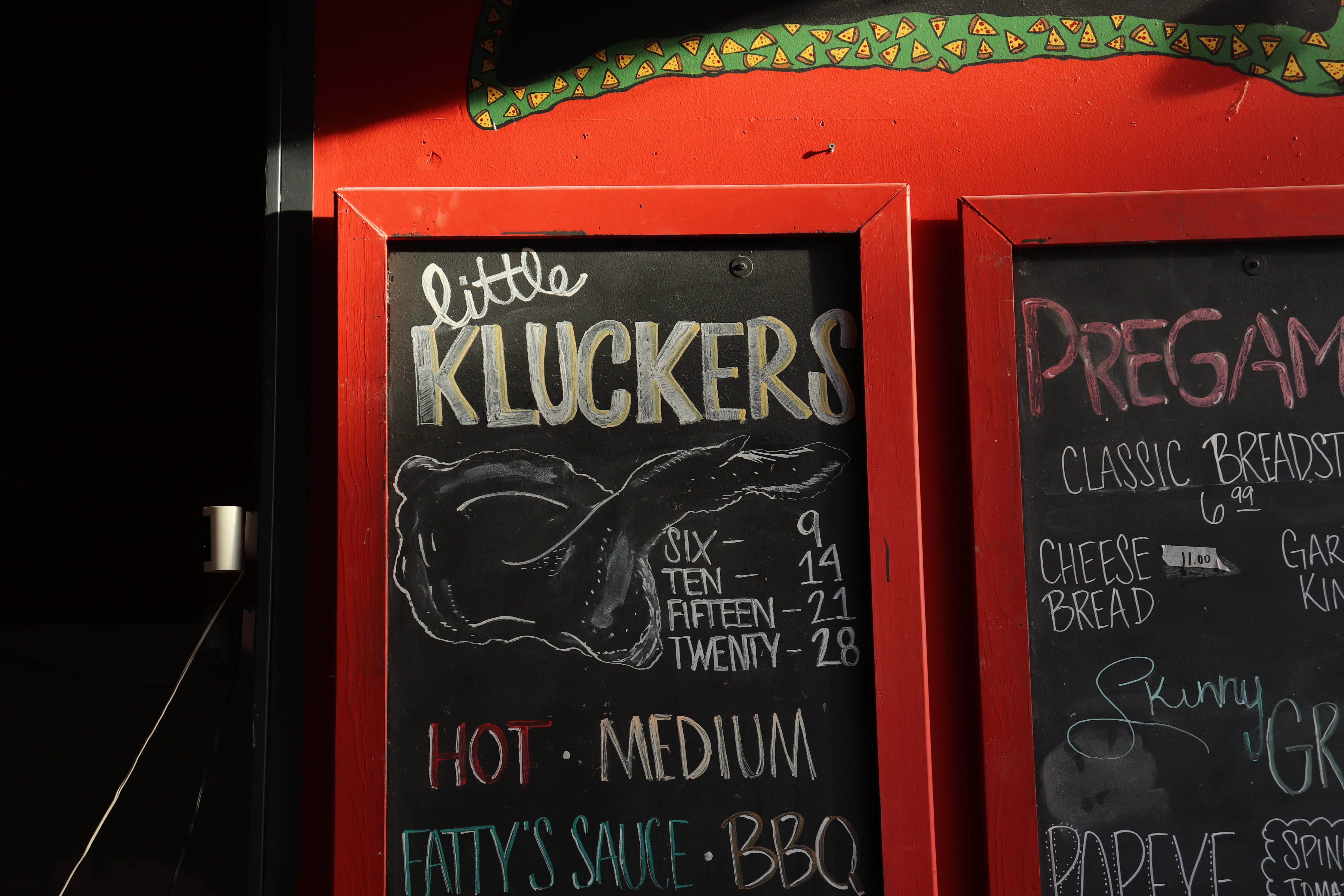 Chalkboard menu with 'Little Kluckers' and prices. Lists hot, medium sauces and BBQ. Classic breadsticks, cheese bread, and spinach tomato options.