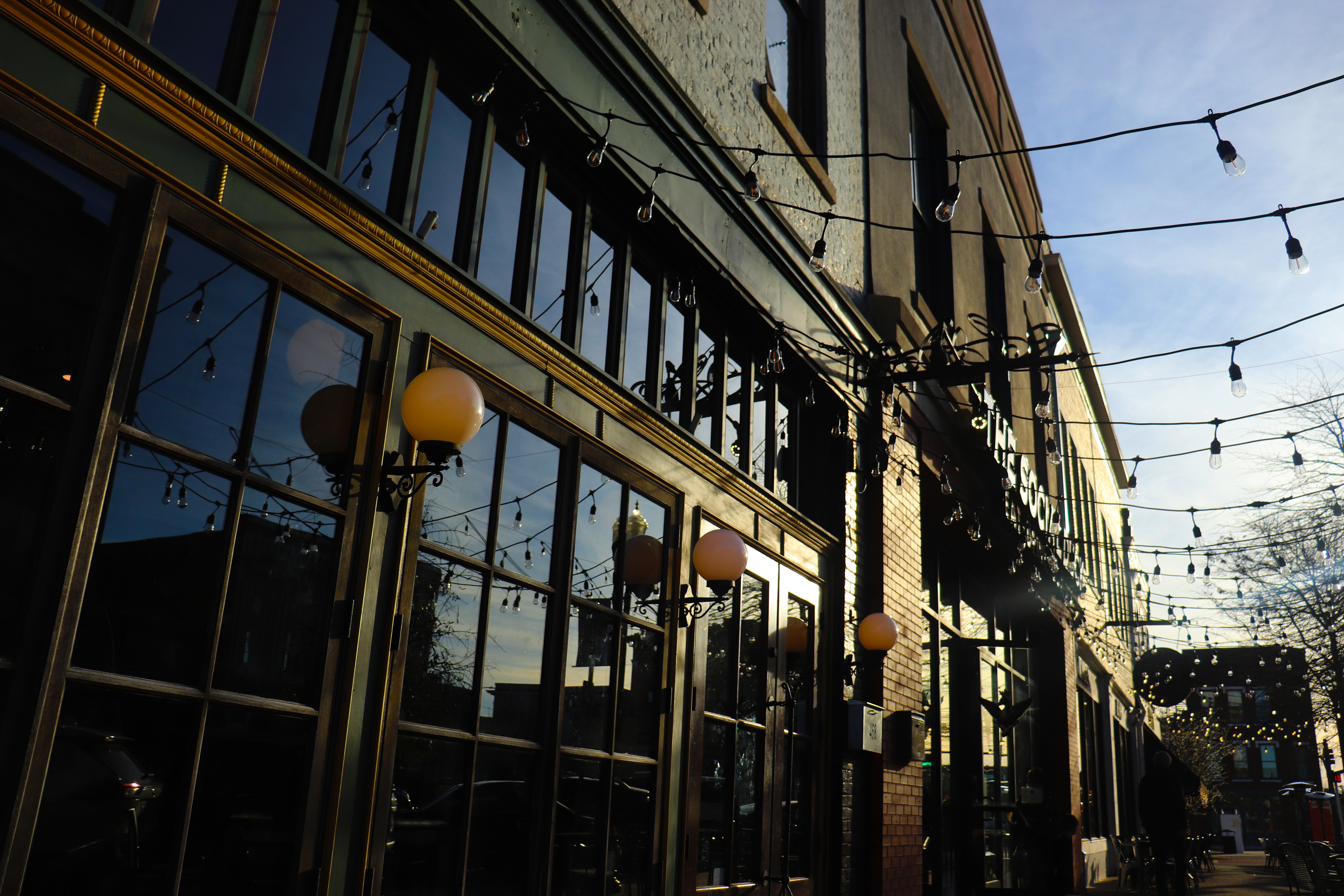 Exterior shot of brick building with large windows and globe-shaped lamps, street-side view with light strands and light bulbs.