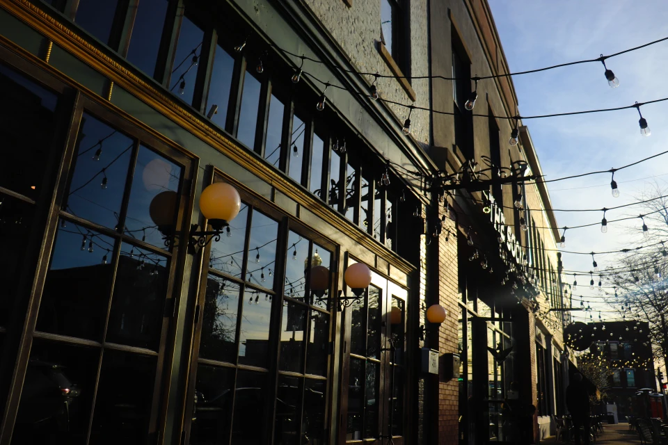 Exterior shot of brick building with large windows and globe-shaped lamps, street-side view with light strands and light bulbs.