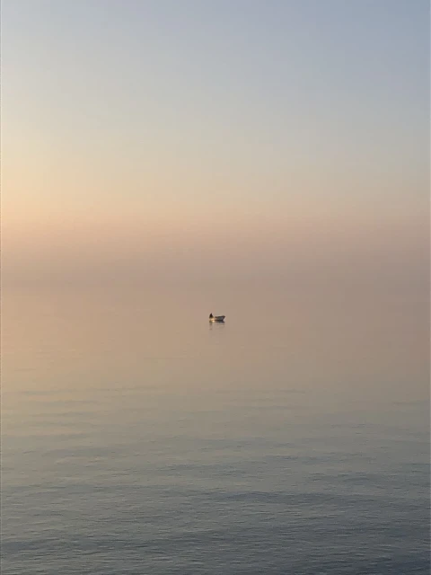 A solitary rowboat floats serenely on calm water at dawn, with soft pastel hues painting the sky in shades of pink and blue.