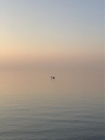 A solitary rowboat floats serenely on calm water at dawn, with soft pastel hues painting the sky in shades of pink and blue.